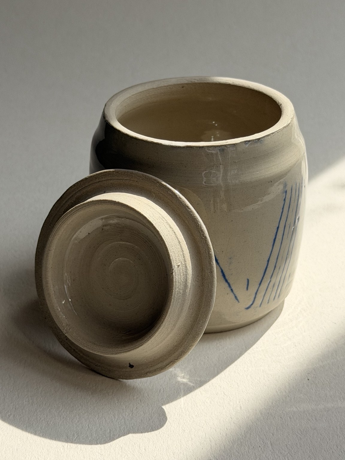 A rounded ceramic jar with its lid resting alongside it